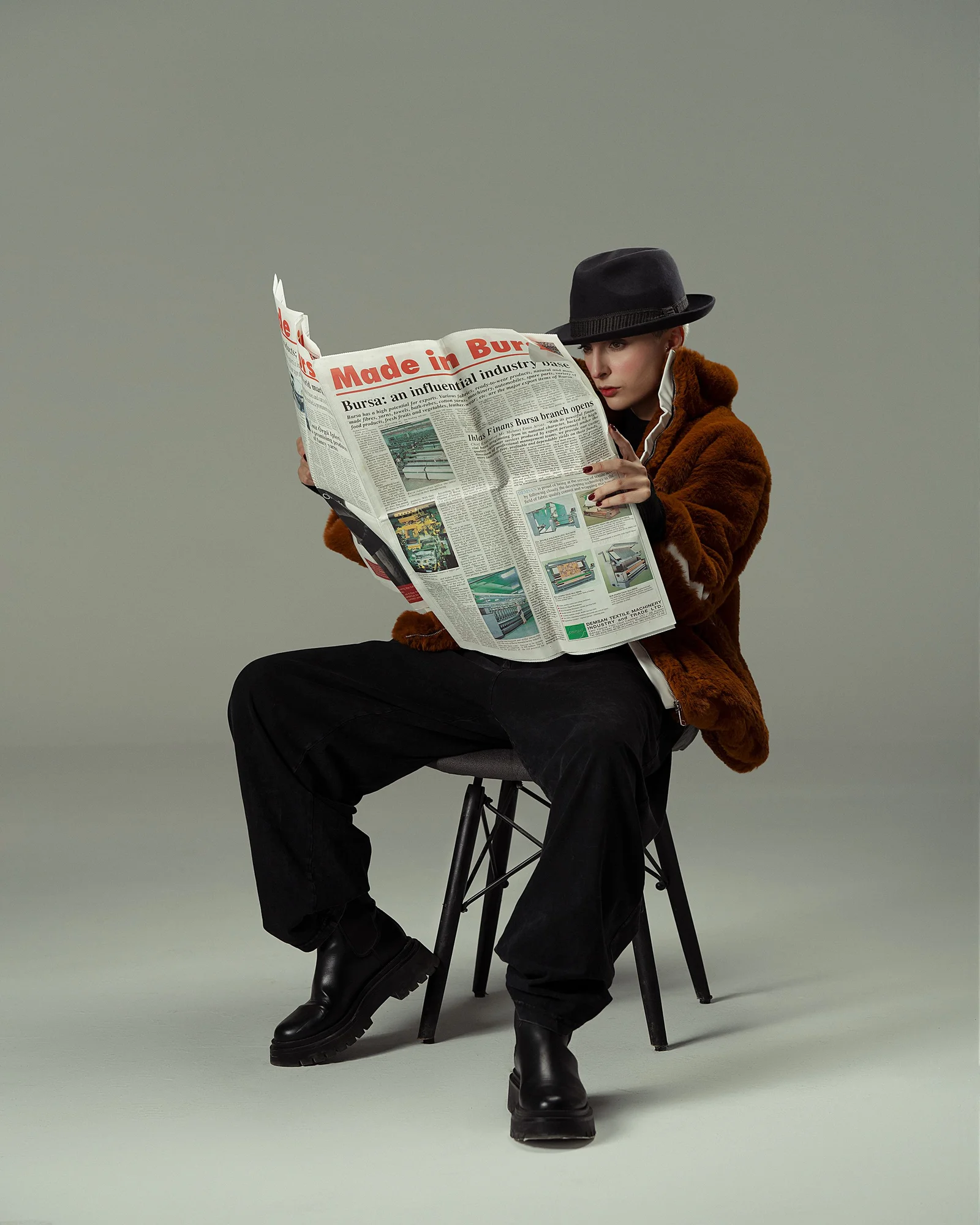 Fashion model in a fedora and fur jacket reading a newspaper